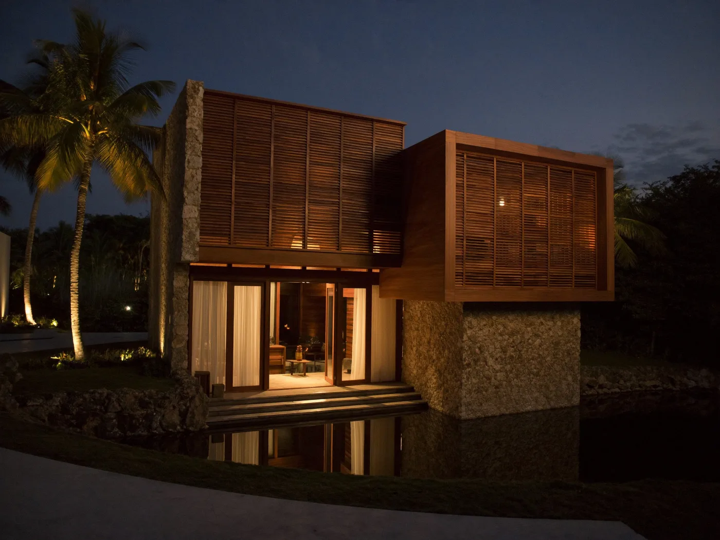 Fachada de villa modernista tropical en madera, piedra y vidrio al atardecer